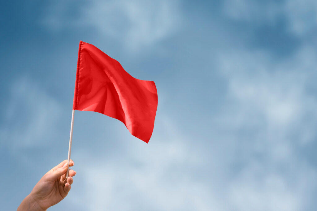 Hand holding a red flag against a blue sky. AML red flag.