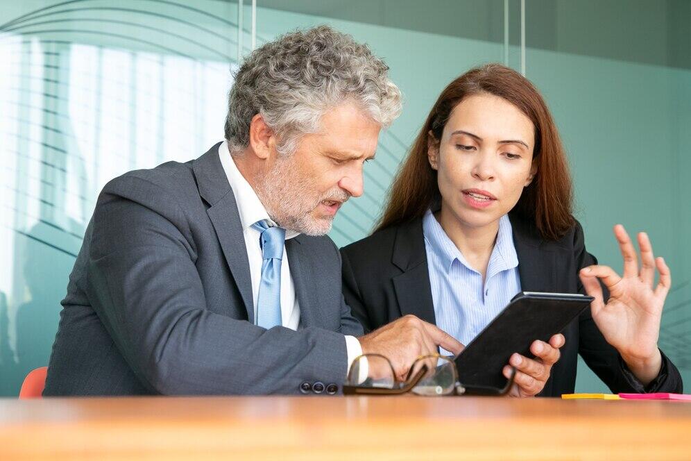 Two business colleagues review a tablet, discussing Australian AML risk assessment guidelines.