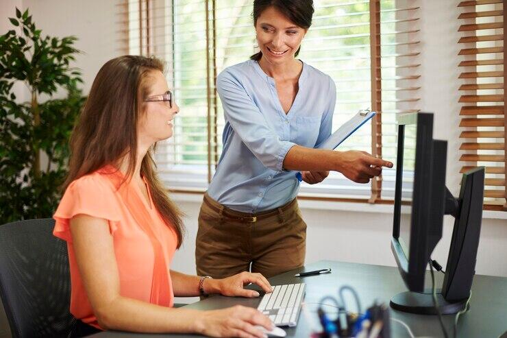 Two businesswomen collaborating on a computer, reviewing documents. Australian AML/CTF compliance.